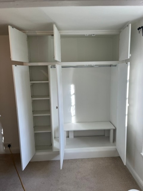 Built-in white wardrobe with its doors open, revealing shelving and desk space